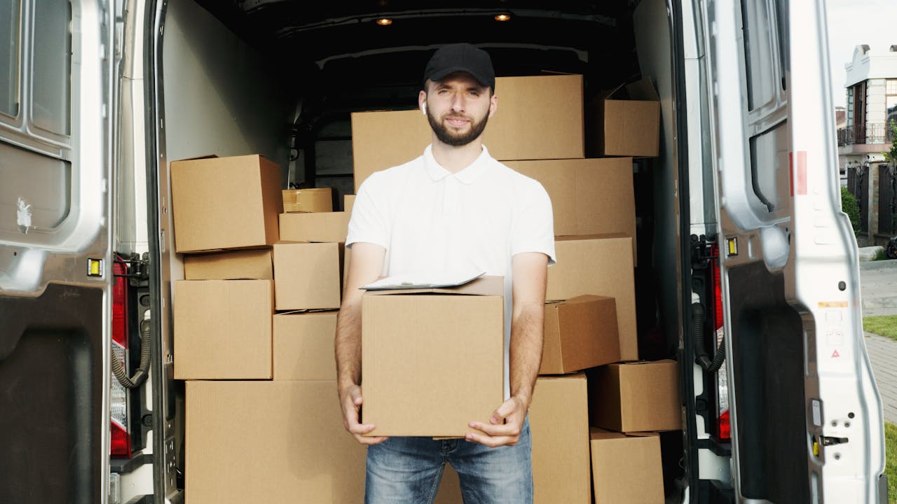 A courier standing at the back of a van holding a package for delivery.
